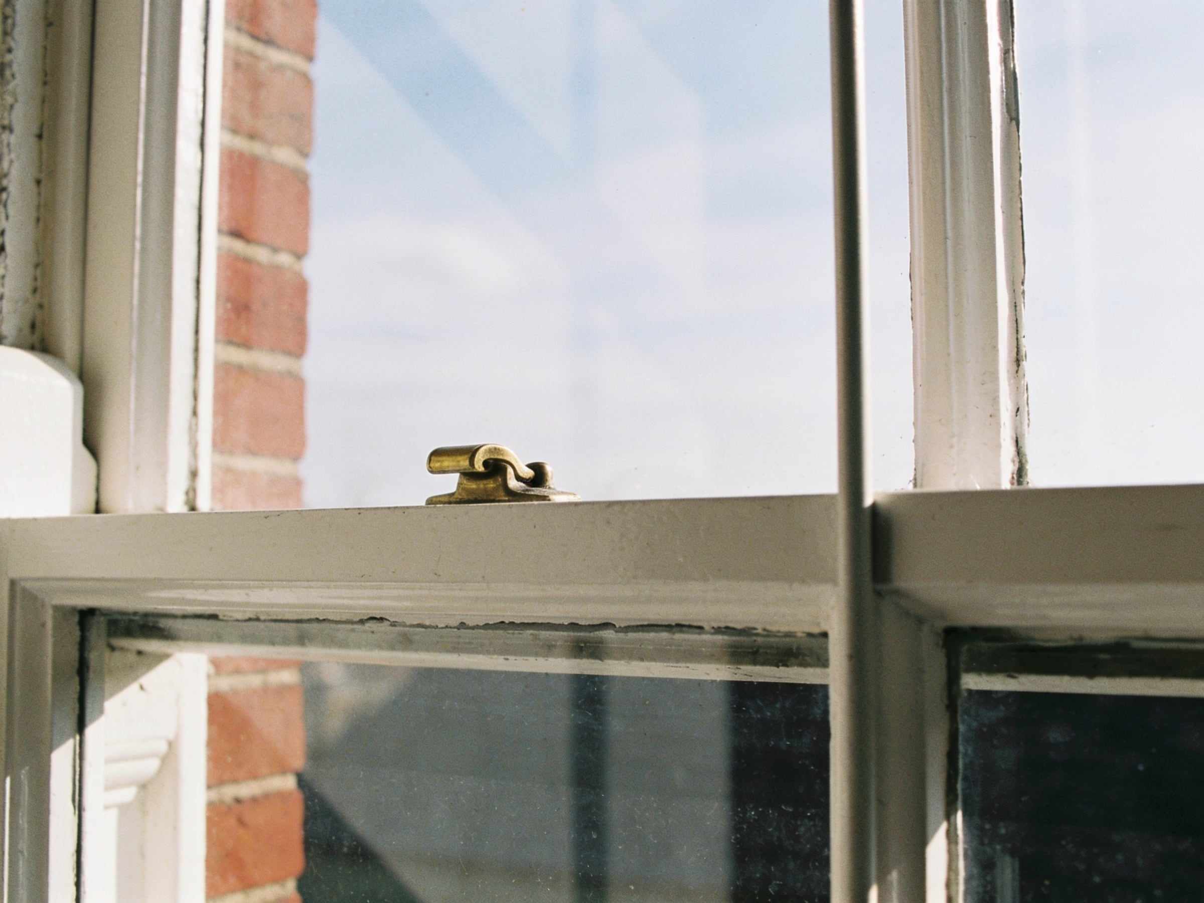 Close-up of a small brass fastener on the meeting rail of a white painted sash window, the sky reflected in the glass and red brick at the edge
