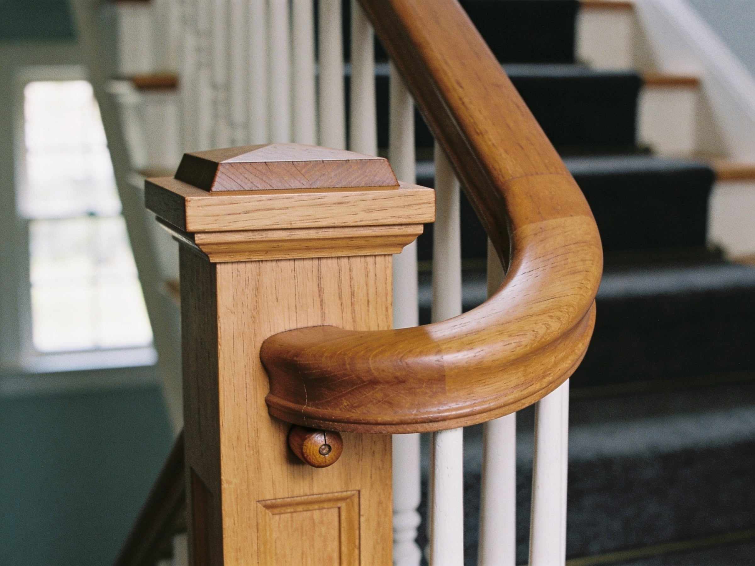 Close-up of an oak newel post with a square cap and a curved oak handrail joining it, held by a round wooden peg