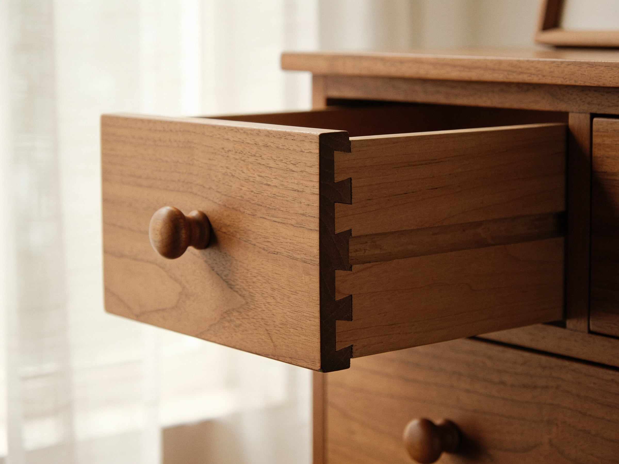 Close-up of a pale oak drawer pulled half open, showing the fine hand-cut dovetails at its front corner and a small turned oak knob